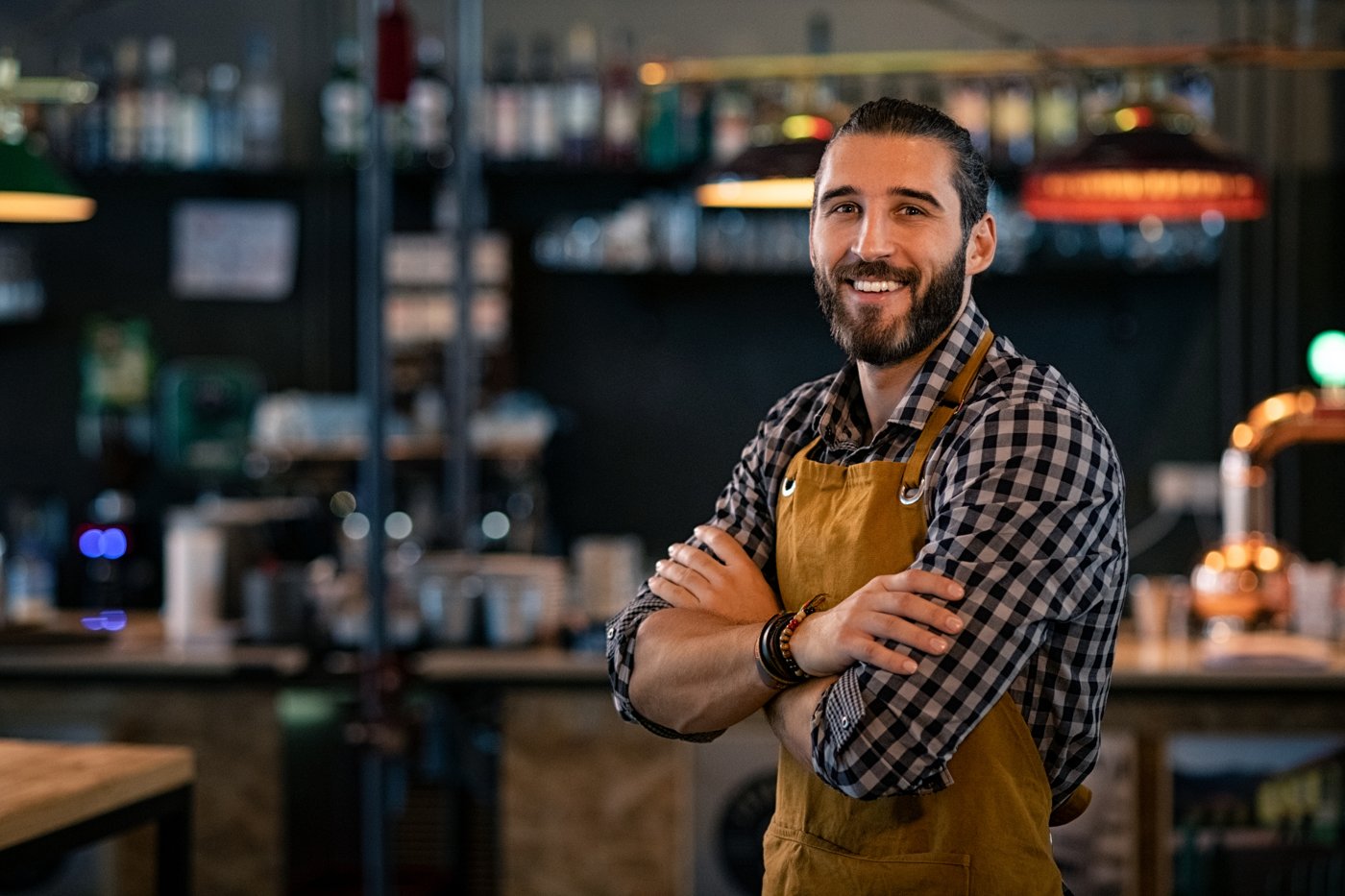 Bartender in apron smiling with arms crossed in front of a bar