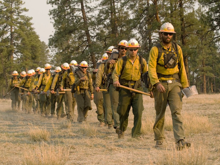 USFS Hot Shot wildland firefighters marching in a line carrying tools in a field