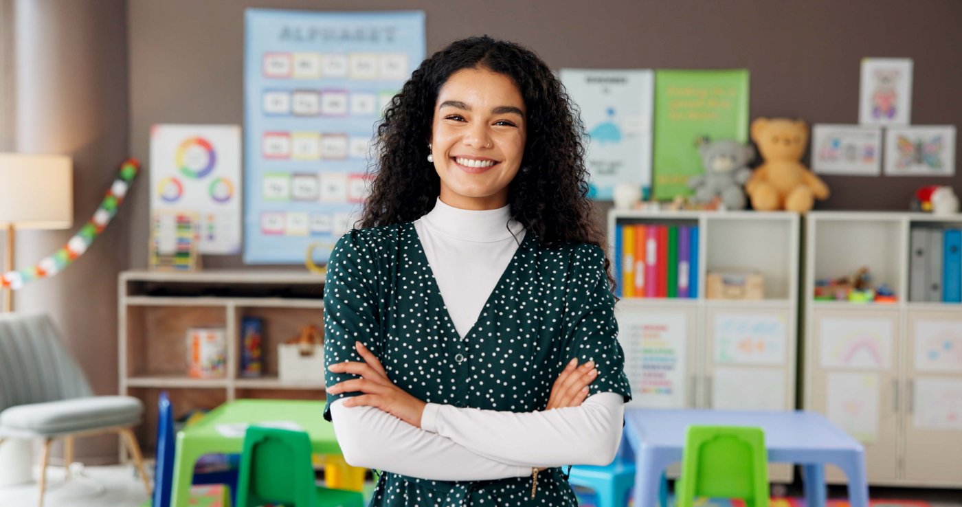 Elementary school teacher smiling with arms crossed in a colorful classroom